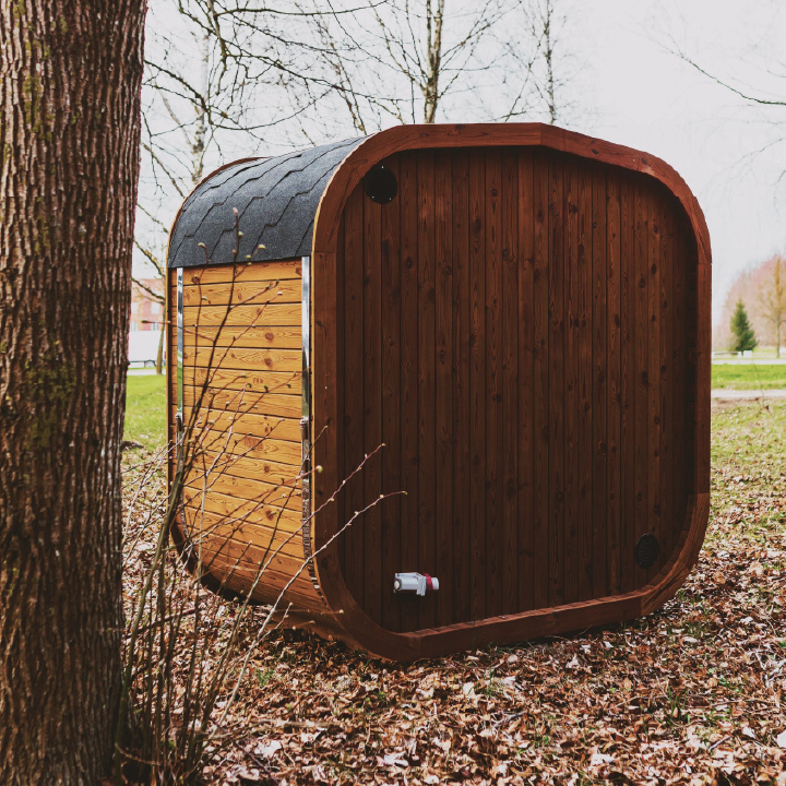 Wooden outdoor sauna pod in a natural setting with trees and grass.