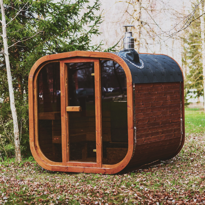 Wooden outdoor sauna showing tiled roof with exhaust on top, front glass w/ glass door set in a natural background